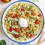 Pesto pasta salad in a white bowl with blue rim with burrata cheese