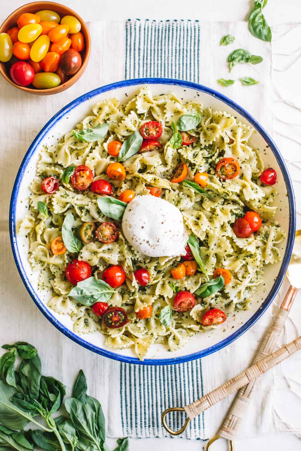 Pesto pasta salad in a white bowl with blue rim with burrata cheese