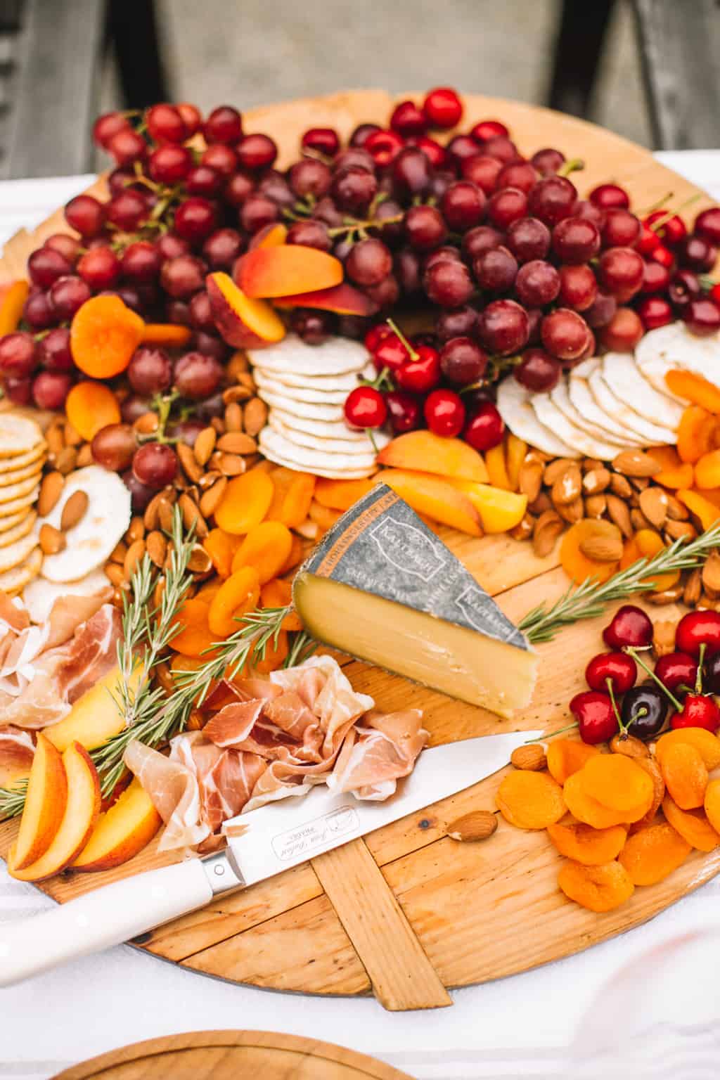 Wooden cheeseboard filled with dried apricots, cherries, grapes, crackers and a wedge of swiss cheese.