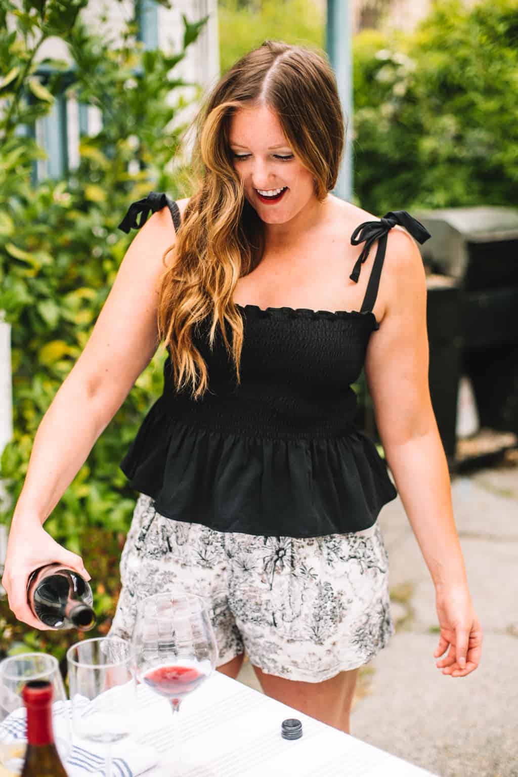 Girl in a black top pouring rosè into a wine glass.