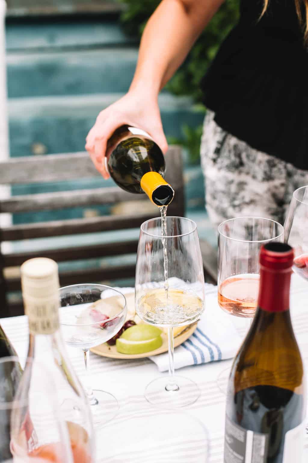 Bottle of white wine being poured into a glass next to other white glasses.