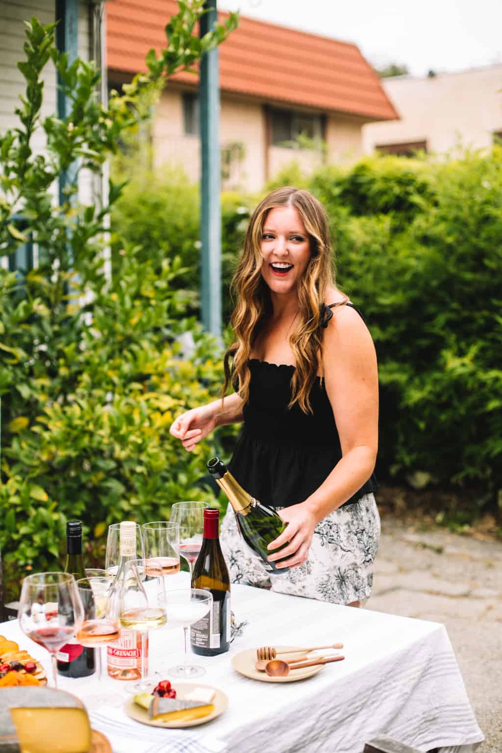 Holding a bottle of champagne on a patio pouring into a glass. 