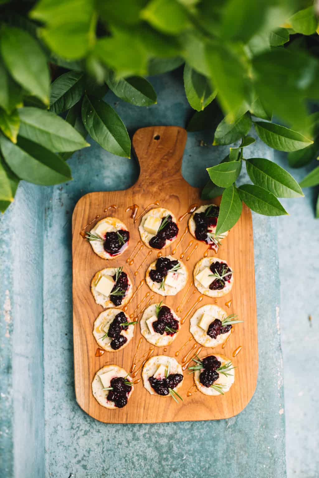 Wooden platter of cracker cheese appetizers with greenery.