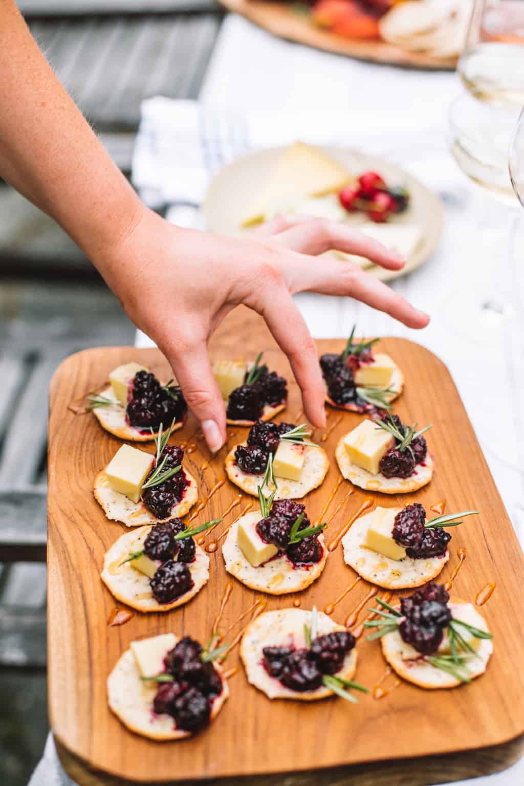 A wooden tray of cracker appetizers topped with swiss cheese and blackberry compote