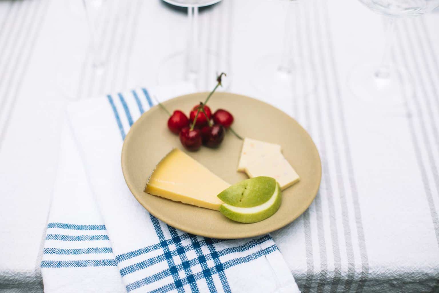 A small tan, ceramic tasting plate with cherries, cheese, apples and white chocolate.