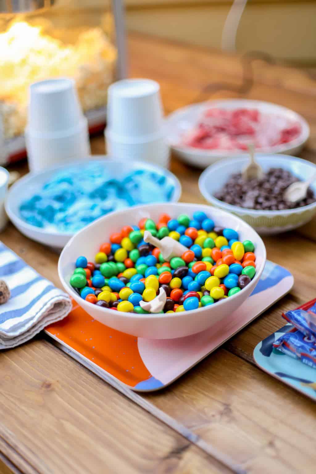 A bowl of colorful MnM's in a pink bowl on a wooden table. 