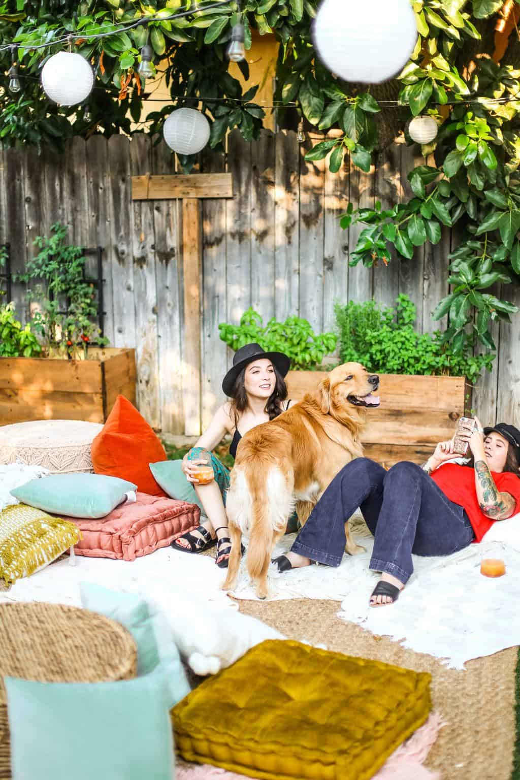 Two girls in a lounge area with a golden retriever at an outdoor movie night party. 