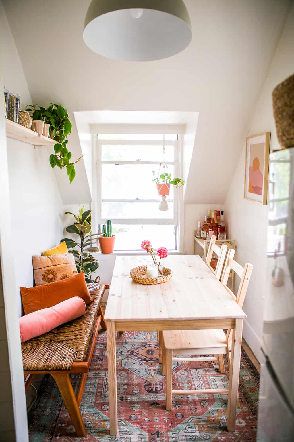 Small dinning room with a wooden table and bench with a rug and bar cart. 