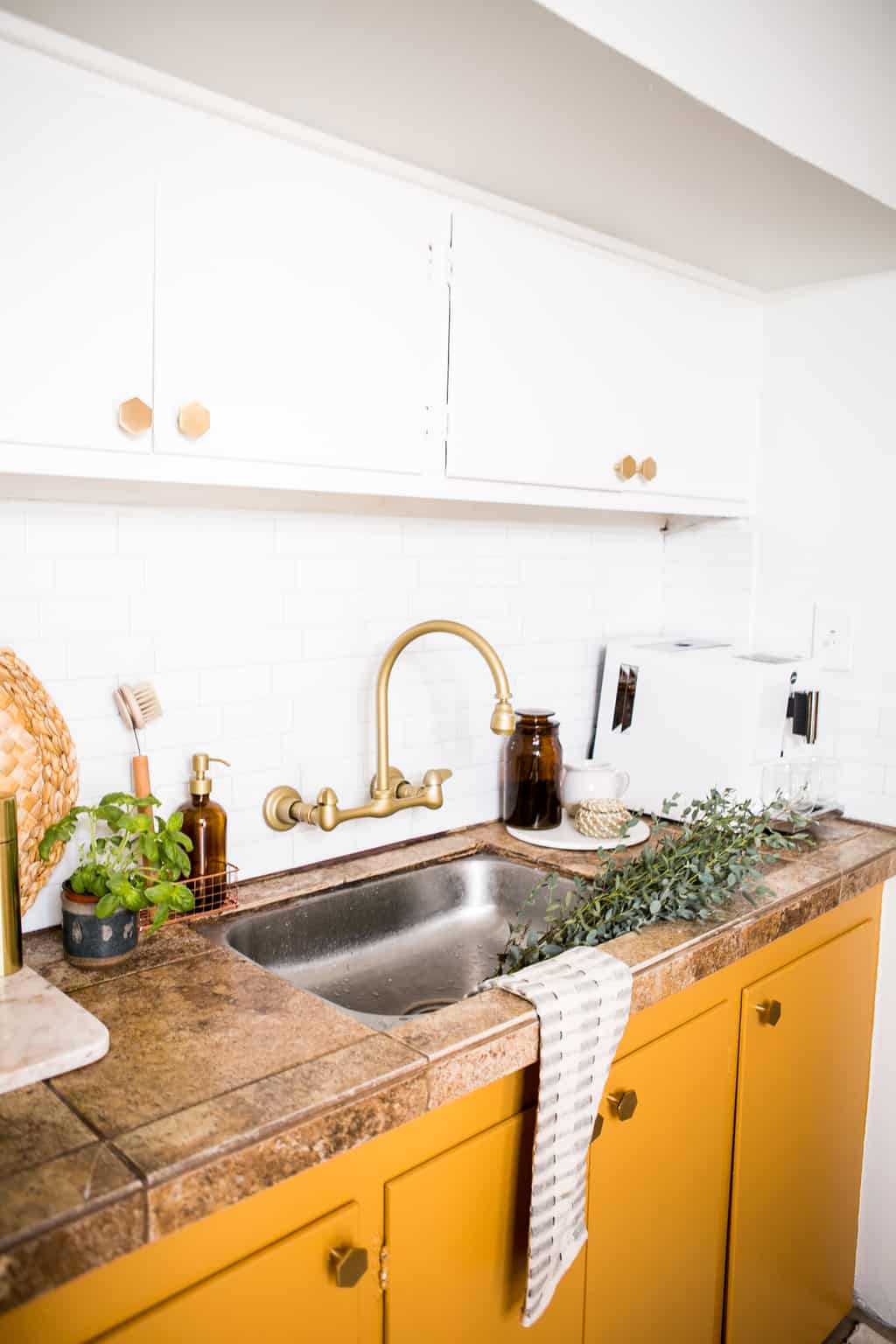 Gold faucet with newly painted yellow mustard cabinets with new gold hardware.