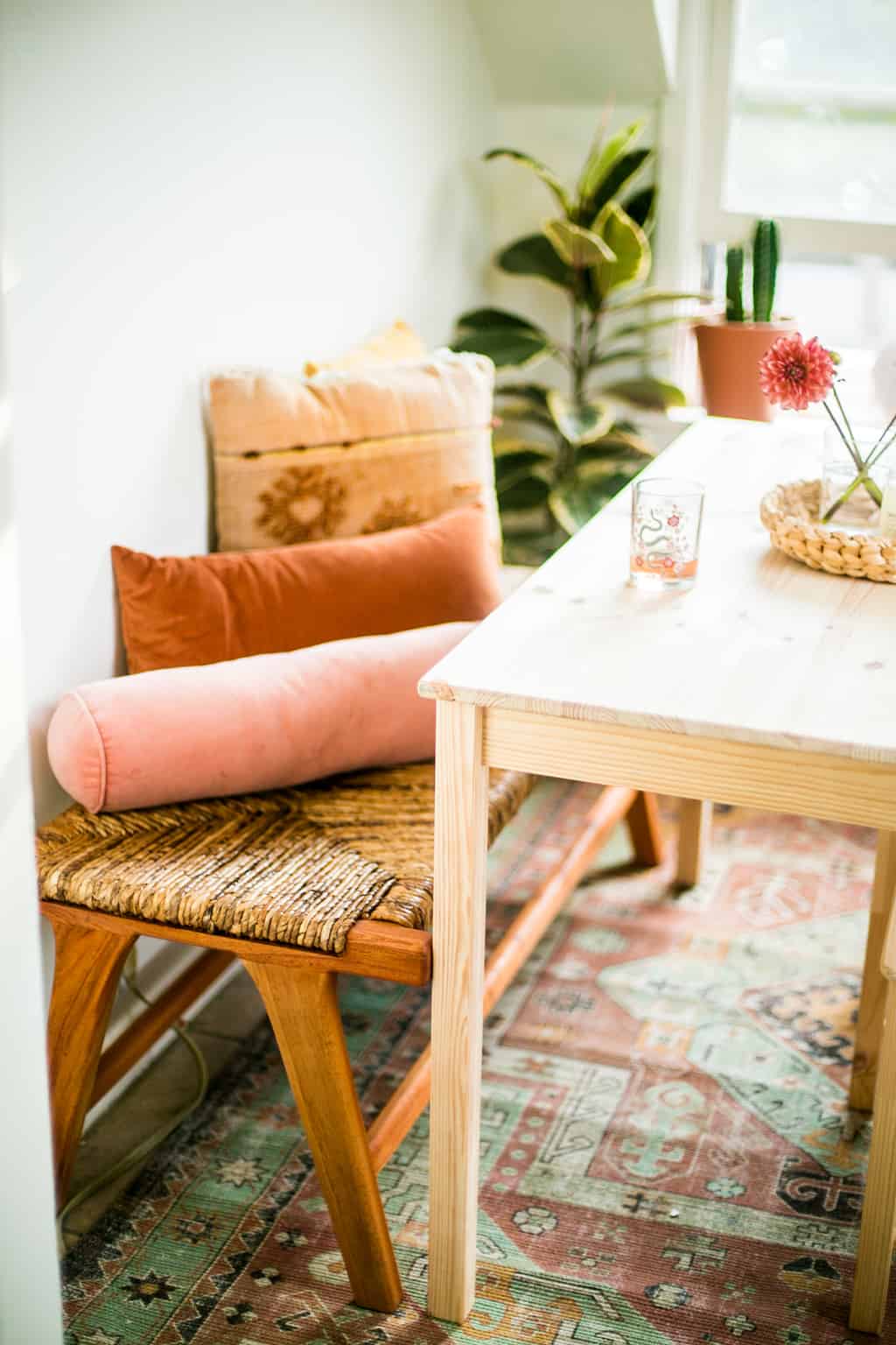 Newly finished dinning room with a small wooden table and a bench with colorful pillows. 