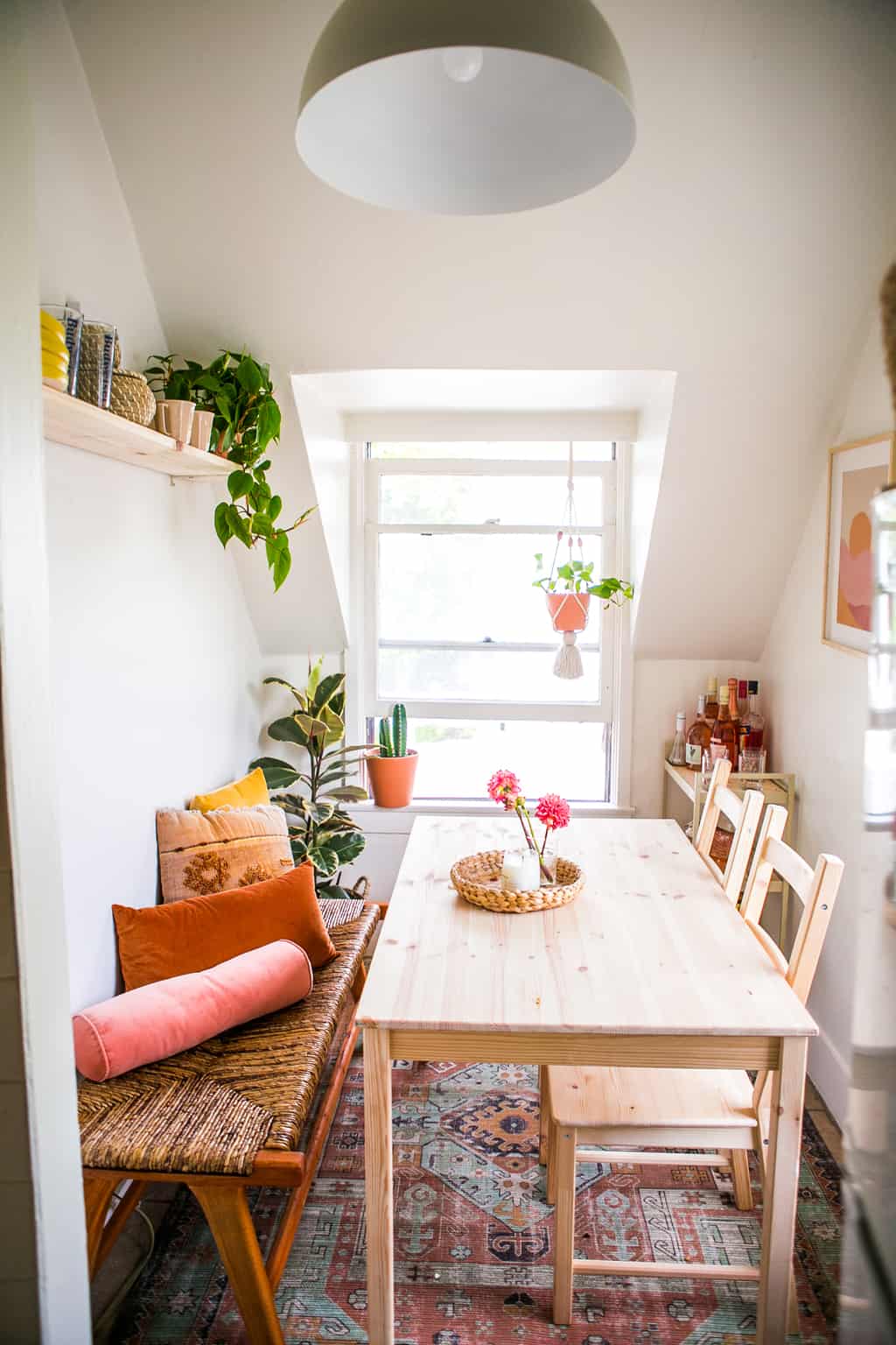 small table with 2 wooden chairs and bench with colorful pillows. 