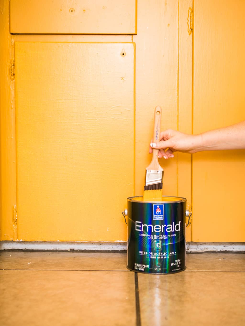 Paint brush with a can of Sherwin Williams paint in front of yellow mustard cabinets. 