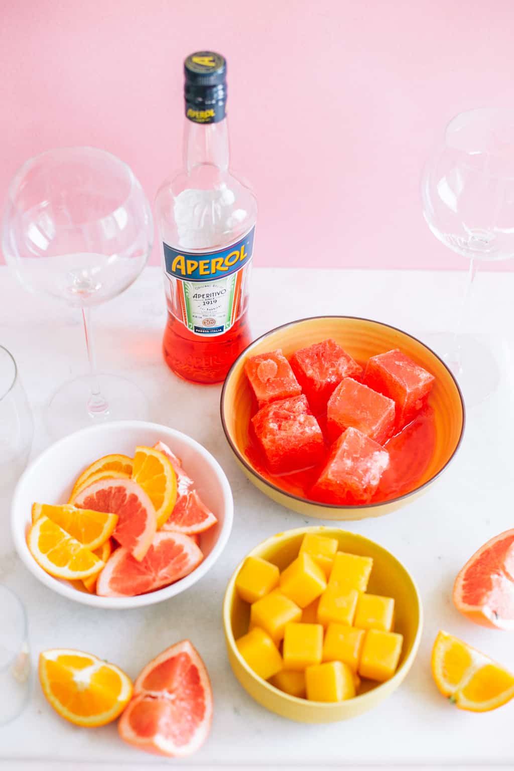 frozen orange juice and aperol ice cubes in two bowls with citrus slices and aperol bottle