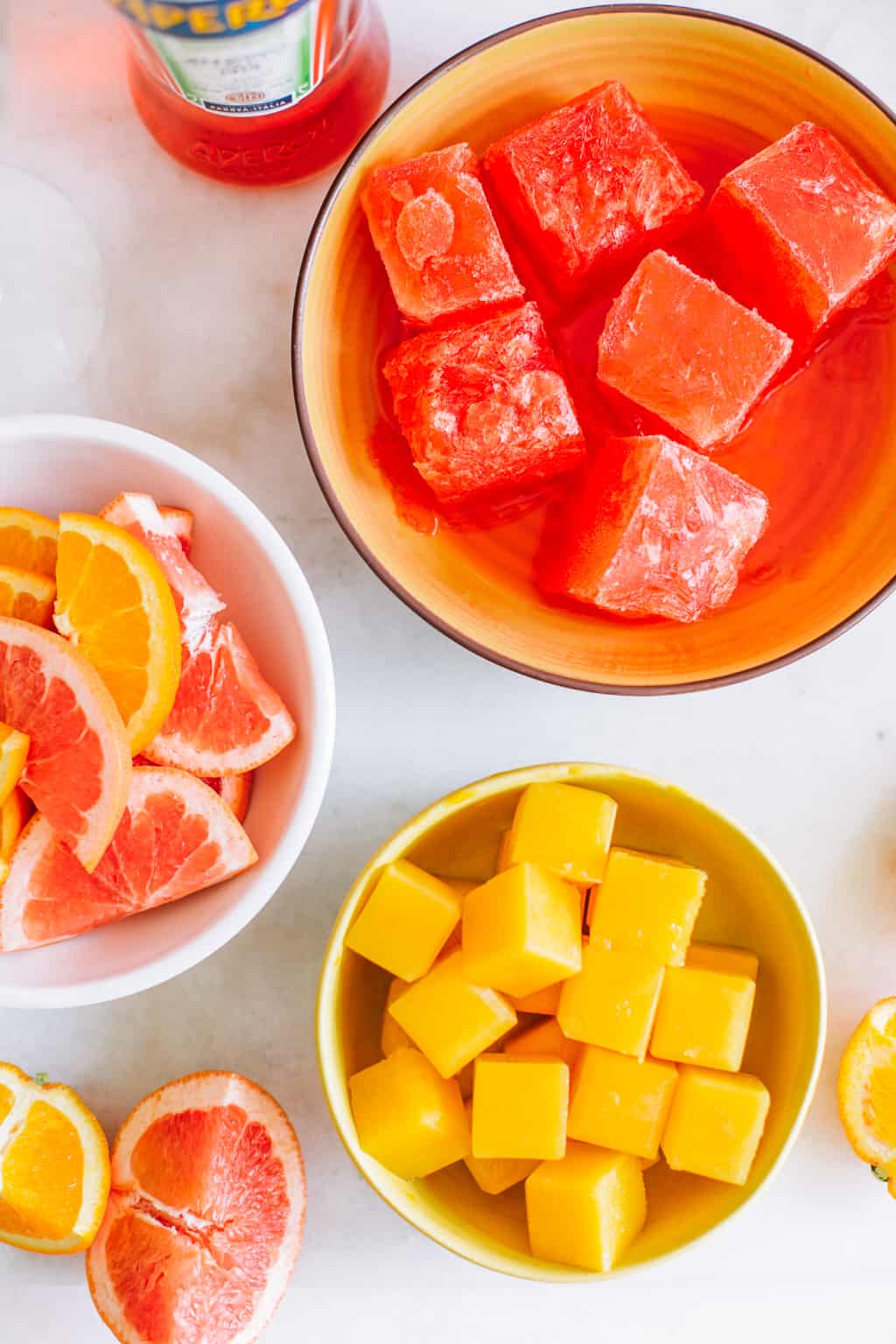 frozen orange juice and aperol ice cubes in two bowls with citrus slices