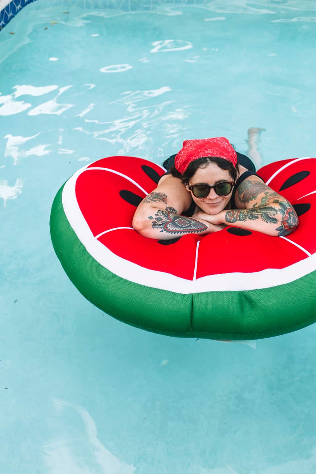 Girl in the pool sitting on a watermelon pool float. 