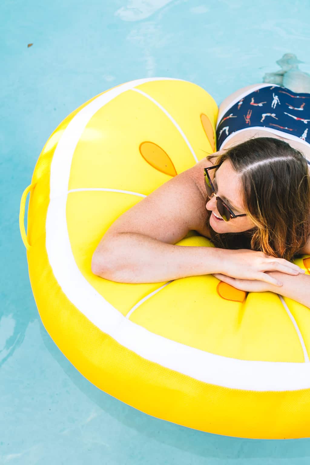 Girl in a bathing suit sitting on a lemon pool float in the pool. 