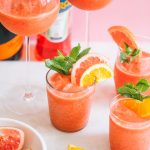 frozen aperol spritz in different glasses and garnished with citrus fruits and mint