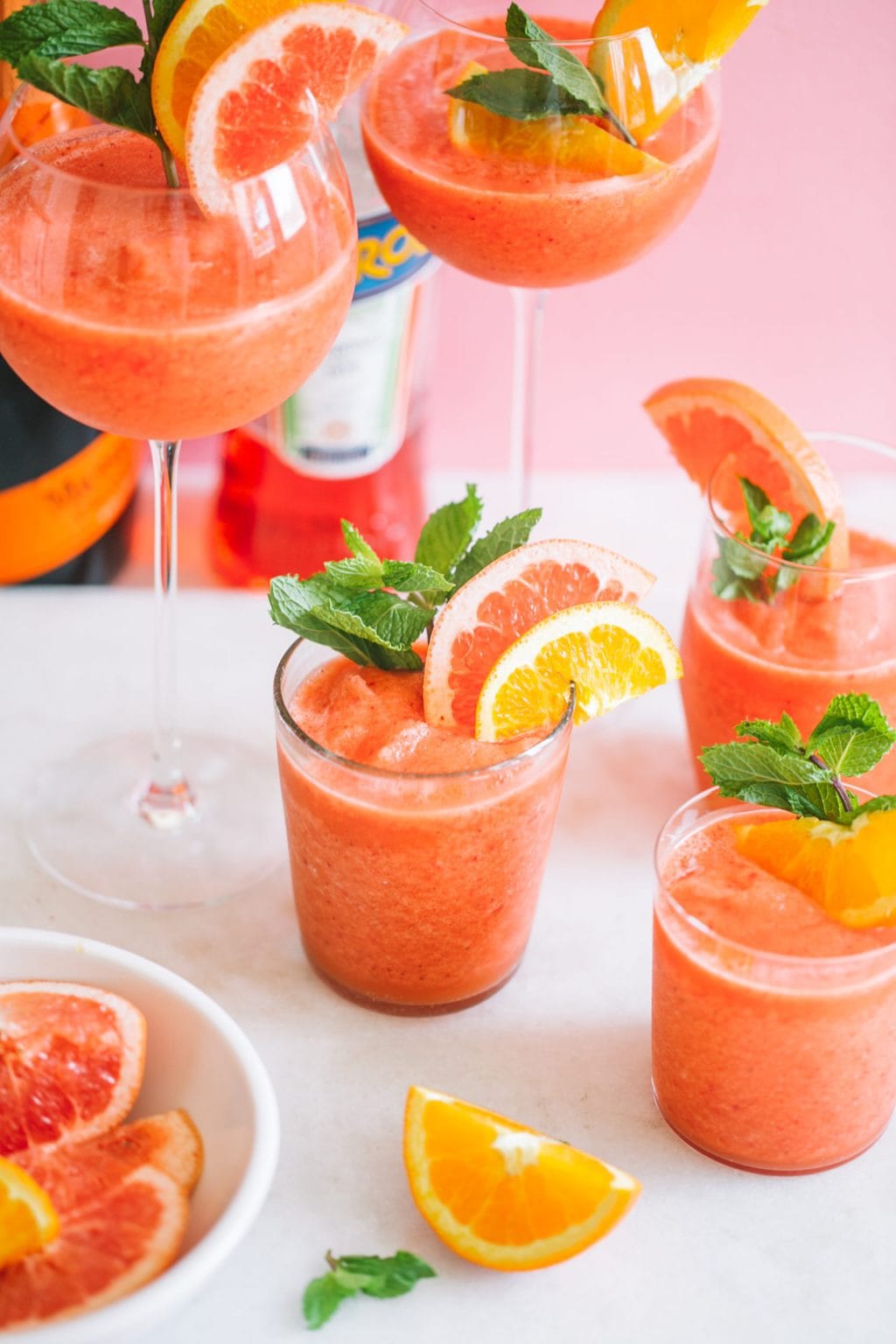 frozen aperol spritz in different glasses and garnished with citrus fruits and mint