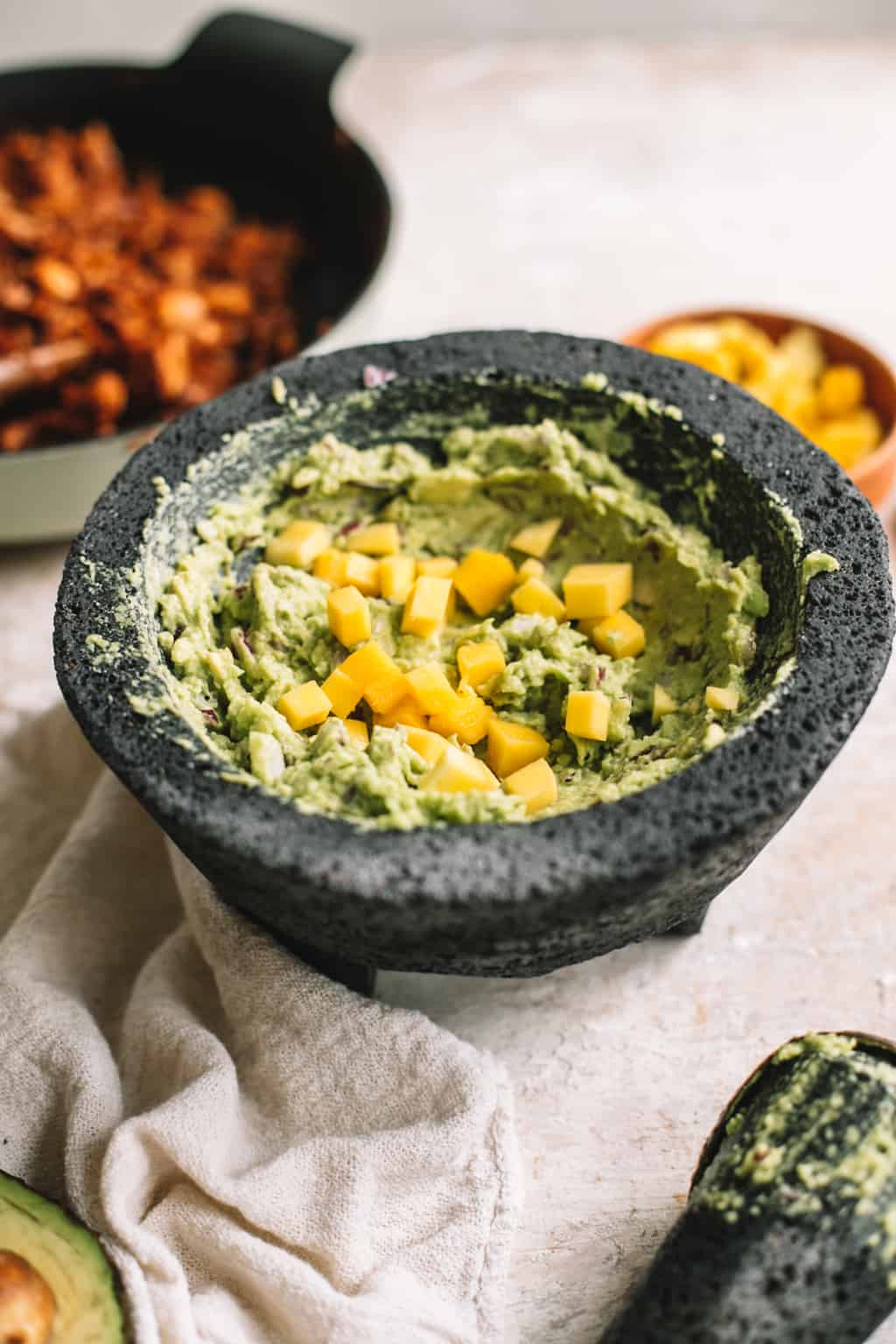 mango guacamole in molcajete with BBQ jackfruit filling in cast iron skillet in background