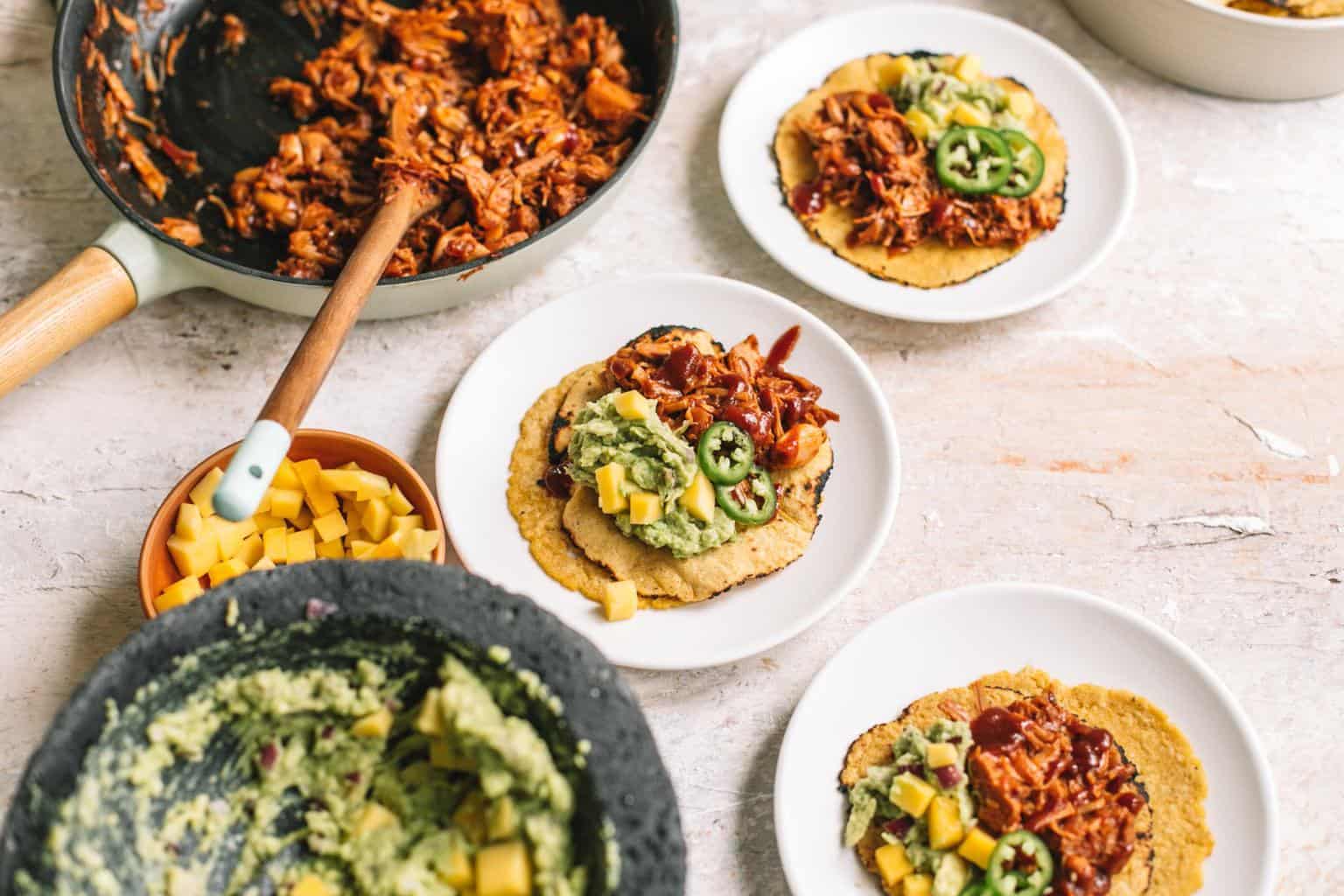 Mexican jackfruit tacos on white plates with BBQ jackfruit filling in cast iron and guacamole