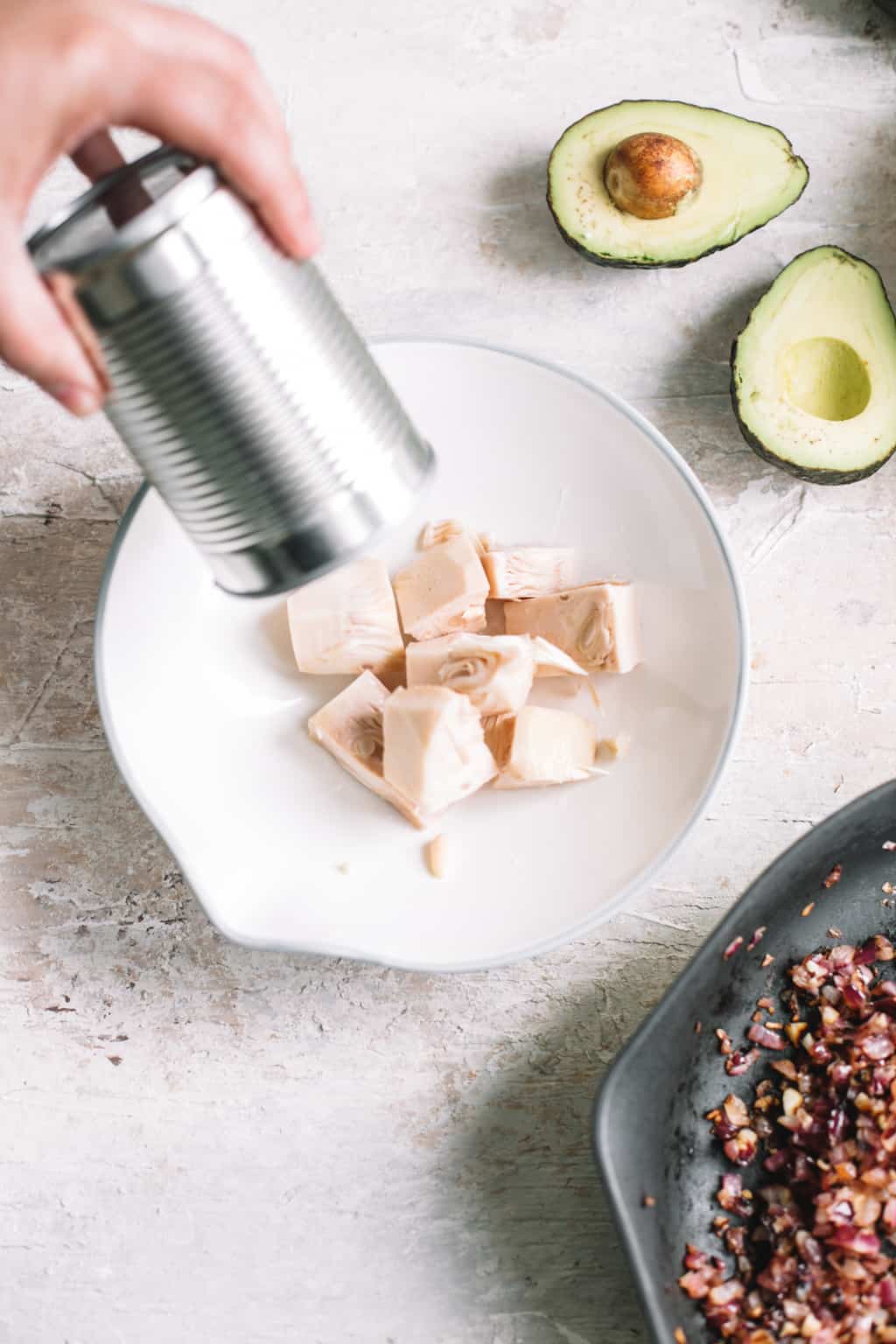 Trader Joe's canned jackfruit being poured into a white bowl with halved avocado on side