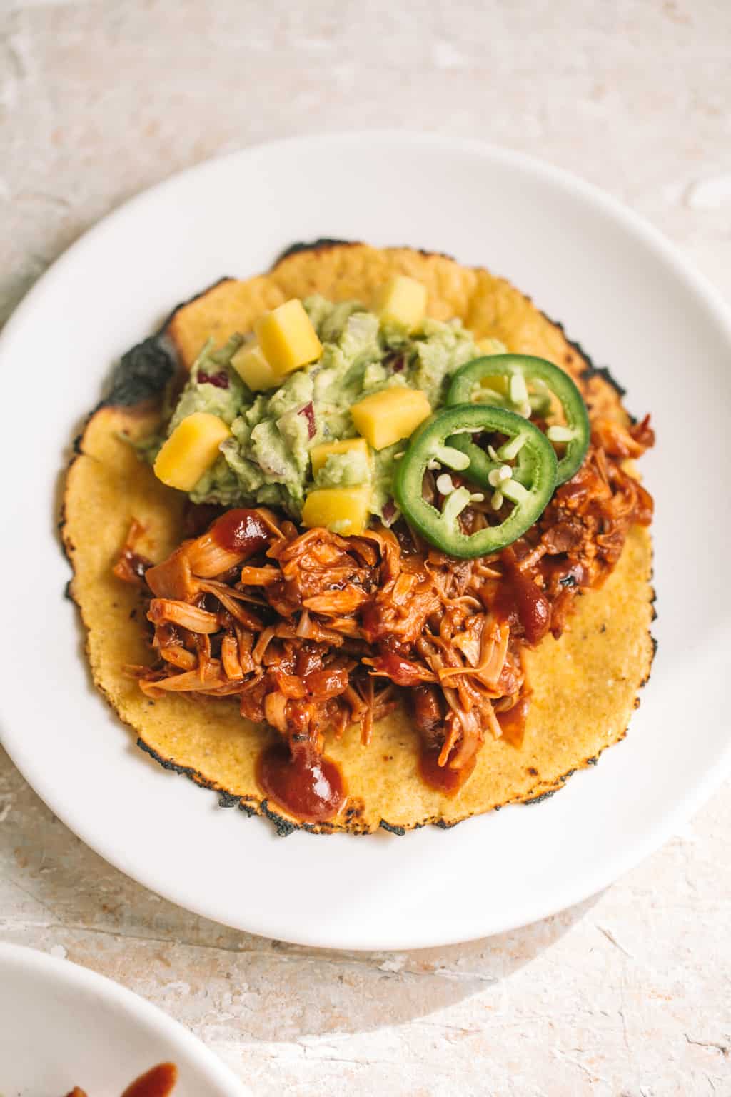 easy chipotle BBQ jackfruit tacos with mango guacamole in corn tortilla on white plate