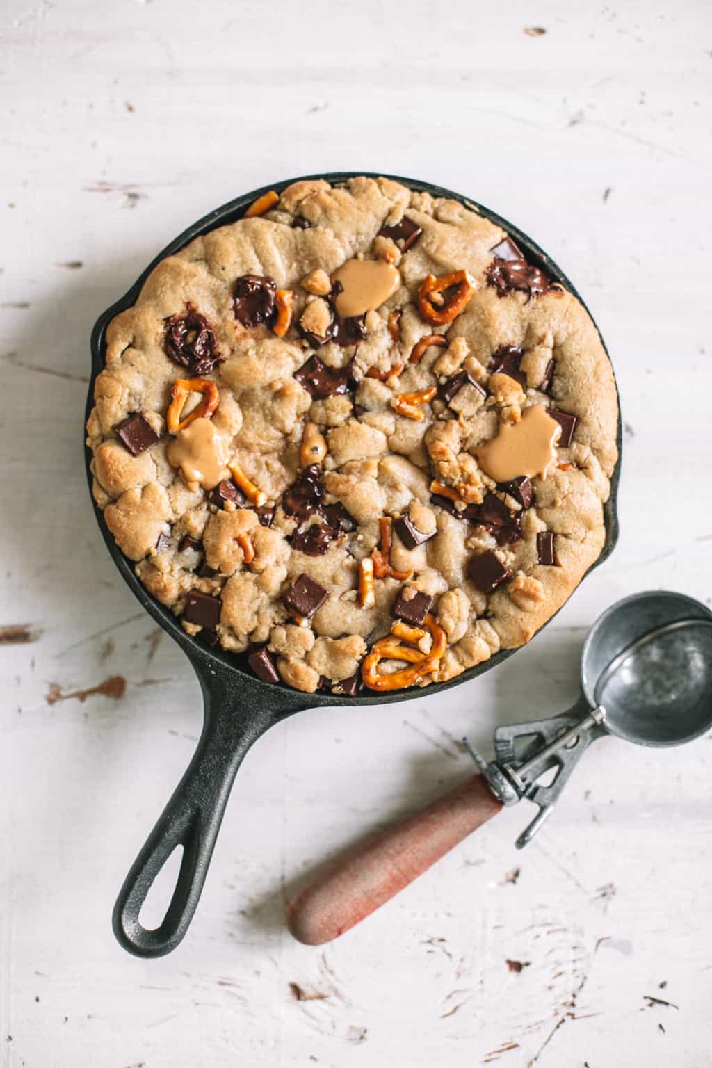 chocolate chip skillet cookie recipe in cast iron with ice cream scoop on white surface