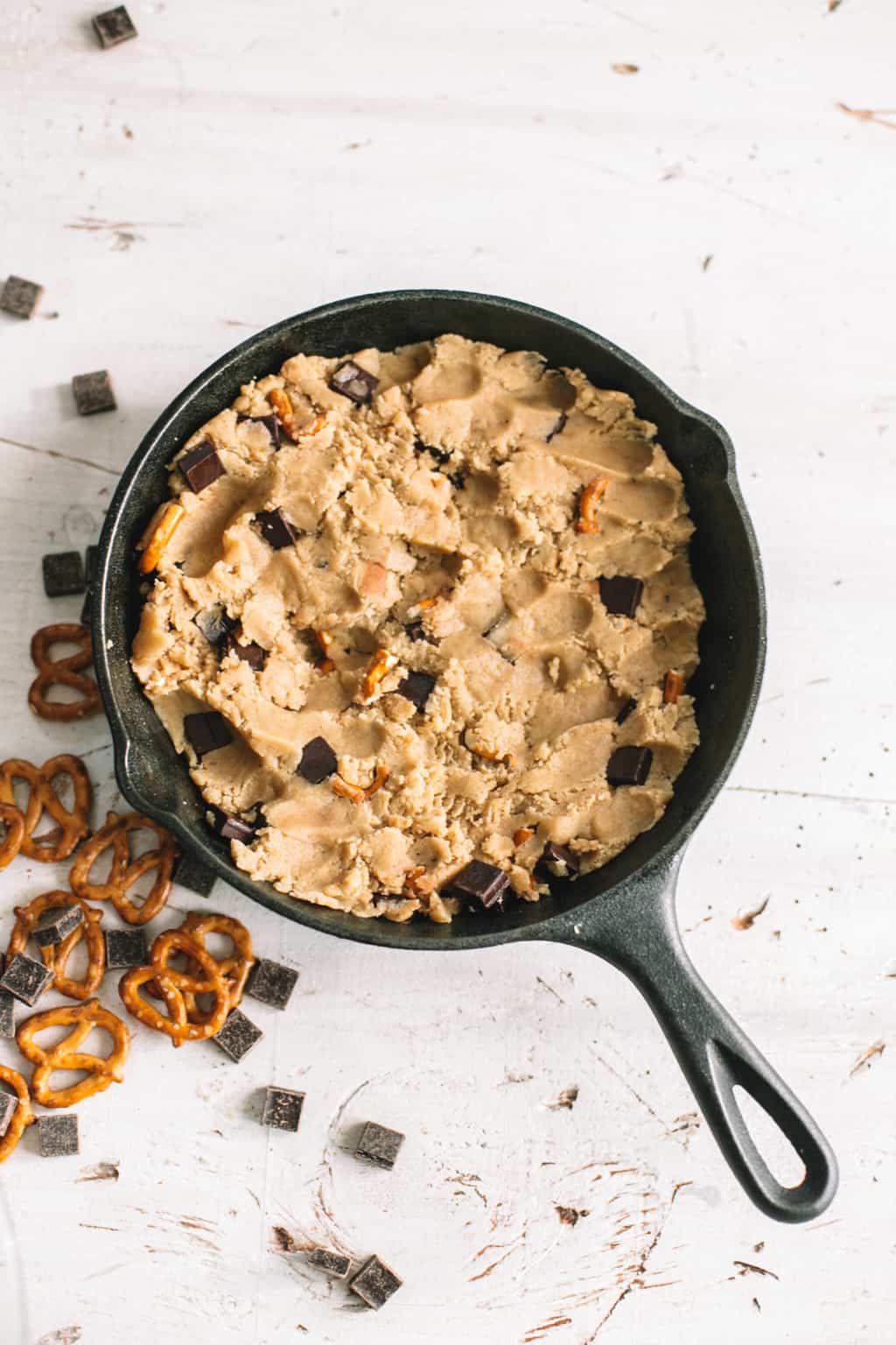 chocolate chip cookie dough in cast iron skillet with pretzels and dark chocolate