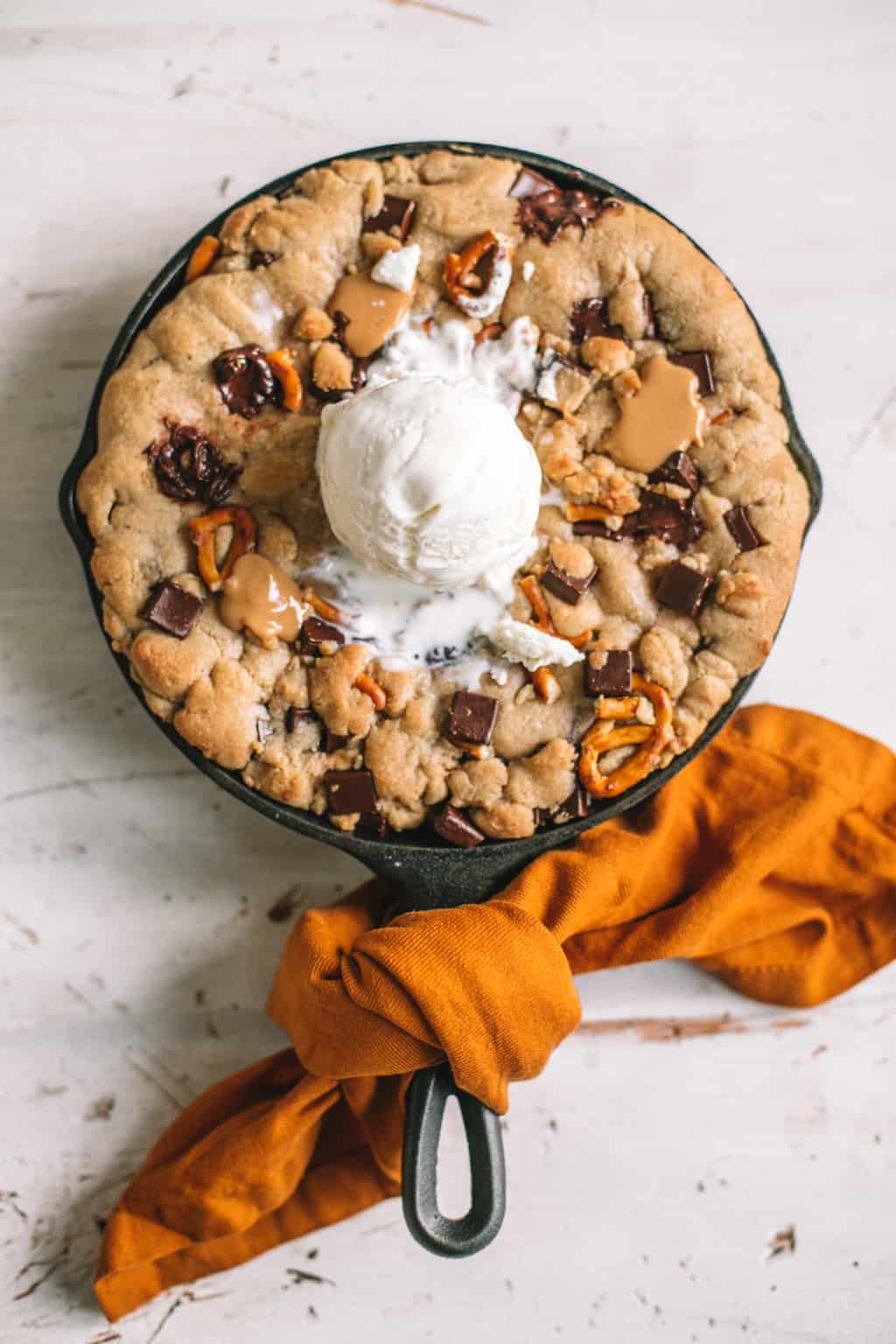 skillet chocolate chip cookie with scoop of vanilla ice cream on top wrapped in gold kitchen towel