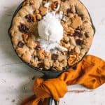 skillet chocolate chip cookie with scoop of vanilla ice cream on top wrapped in gold kitchen towel