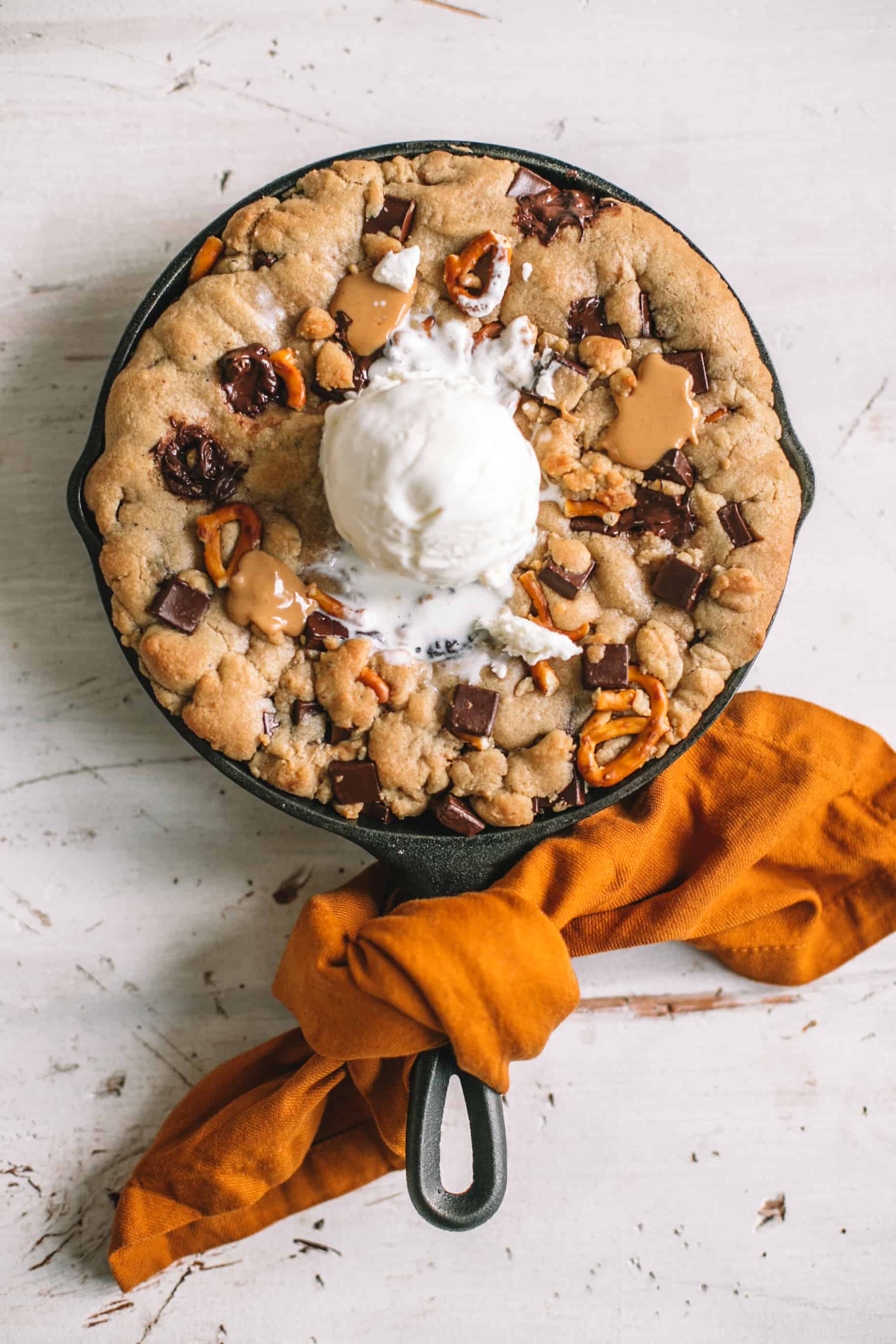 skillet chocolate chip cookie with scoop of vanilla ice cream on top wrapped in gold kitchen towel