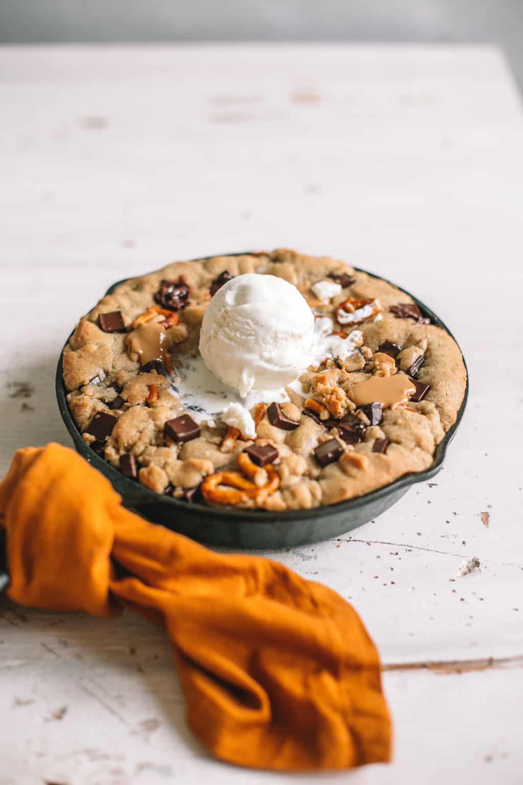 skillet chocolate chip cookie with scoop of vanilla ice cream on top wrapped in gold kitchen towel