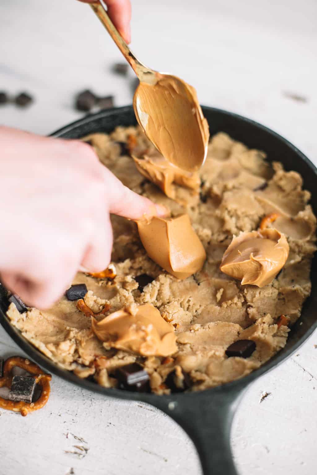 peanut butter being spooned onto chocolate chip cookie dough in cast iron skillet