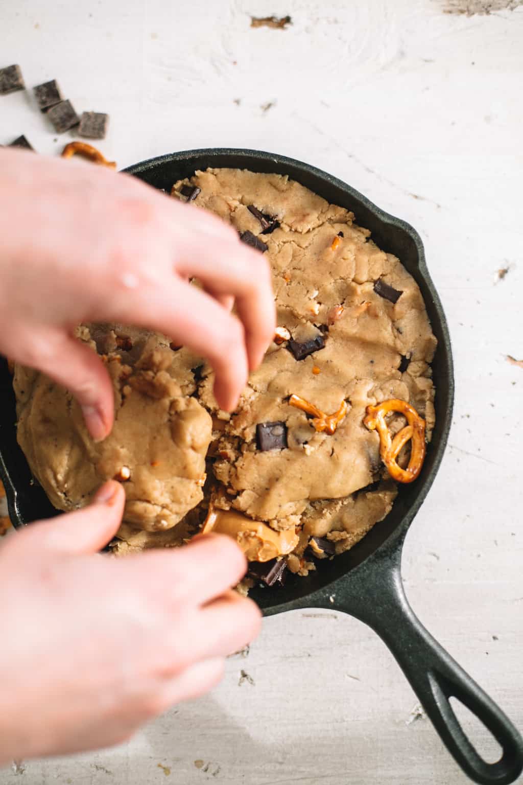 two hand placing chocolate chip cookie dough in cast iron skillet