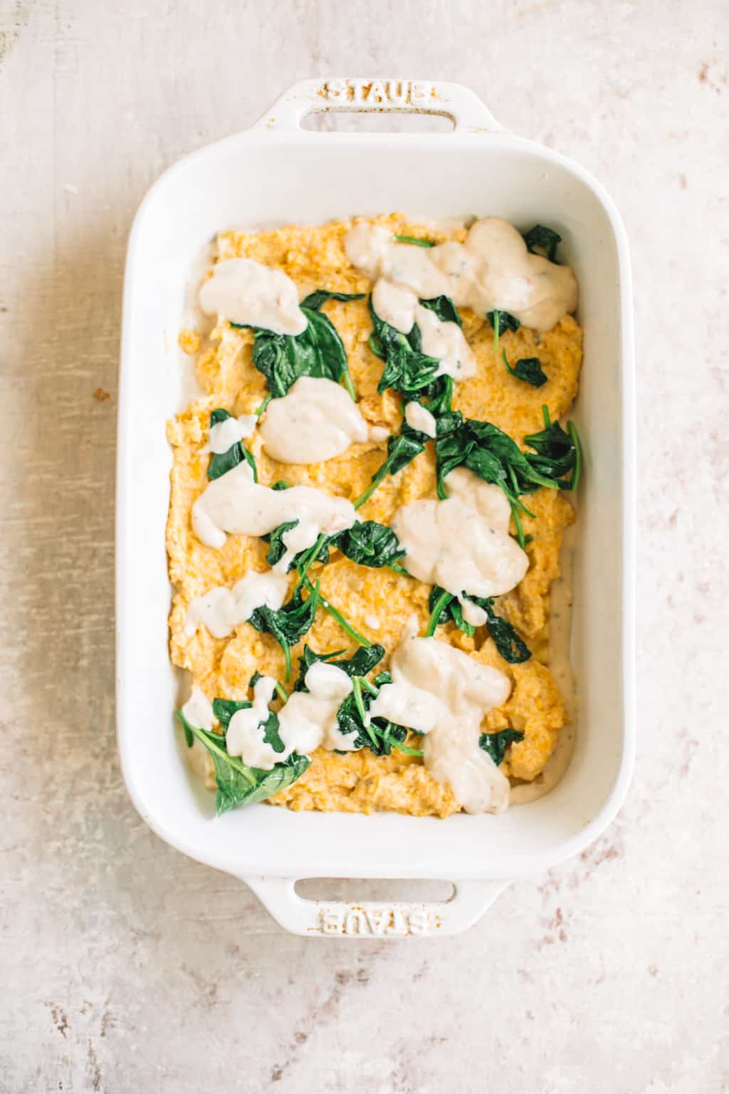 Lasagna in a white casserole dish being layered with cheese, butternut squash ricotta filling, spinach and white sauce. 