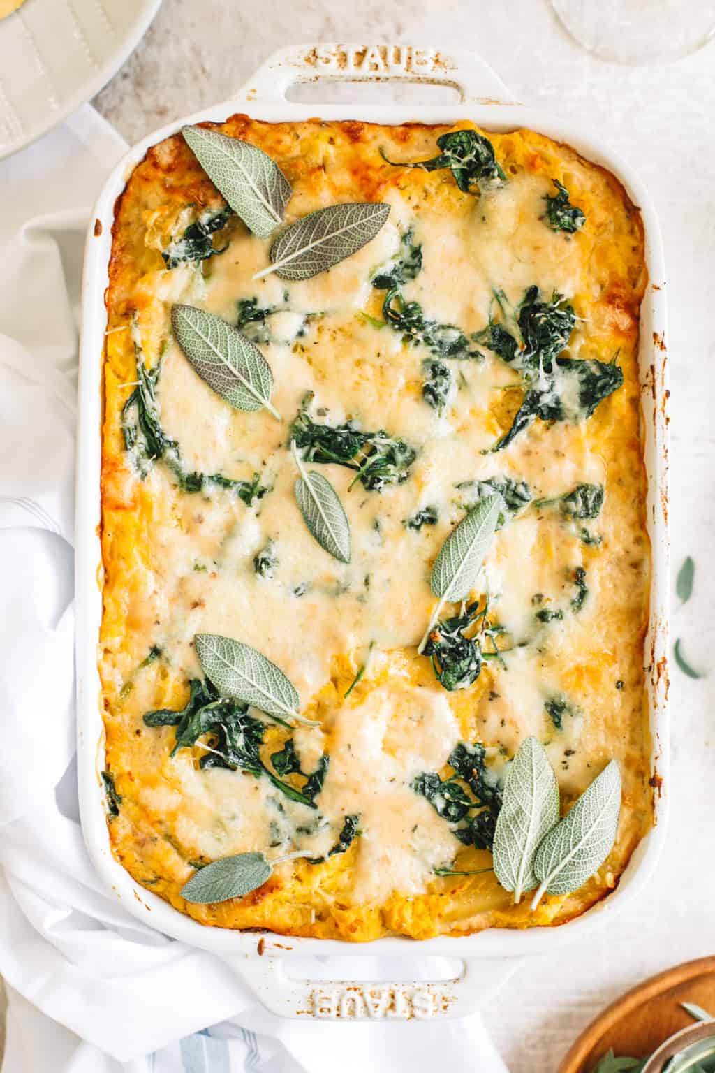 White lasagna topped with sage leaves and melted cheese in a white casserole dish. 