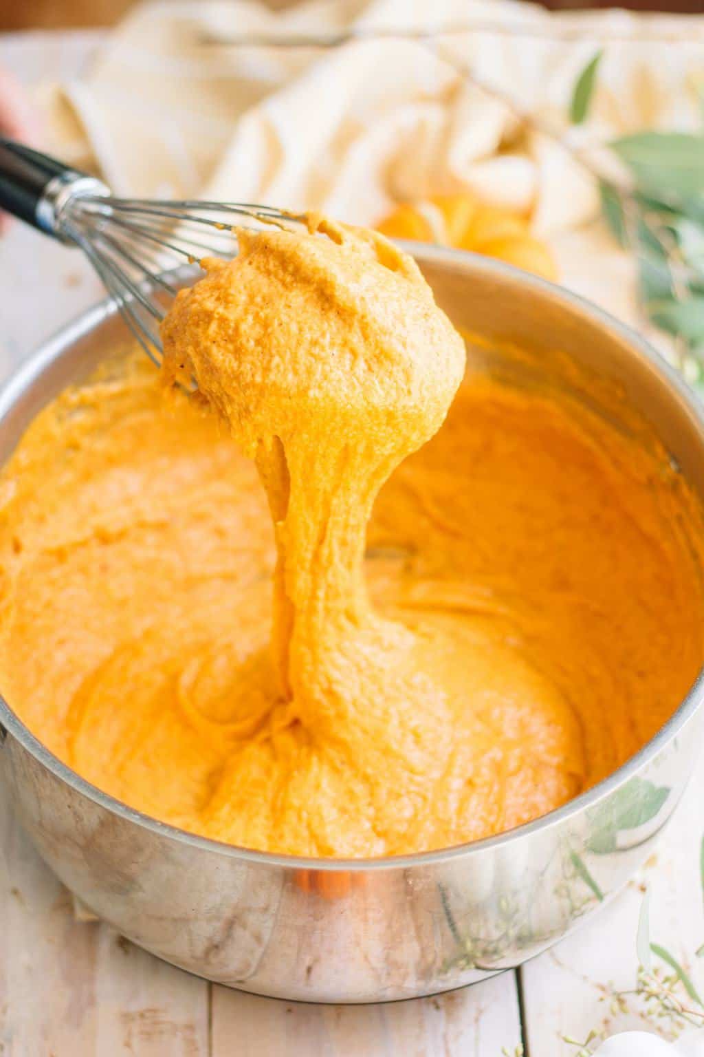 A whisk full of cheesy, pumpkin sauce for pumpkin mac and cheese.