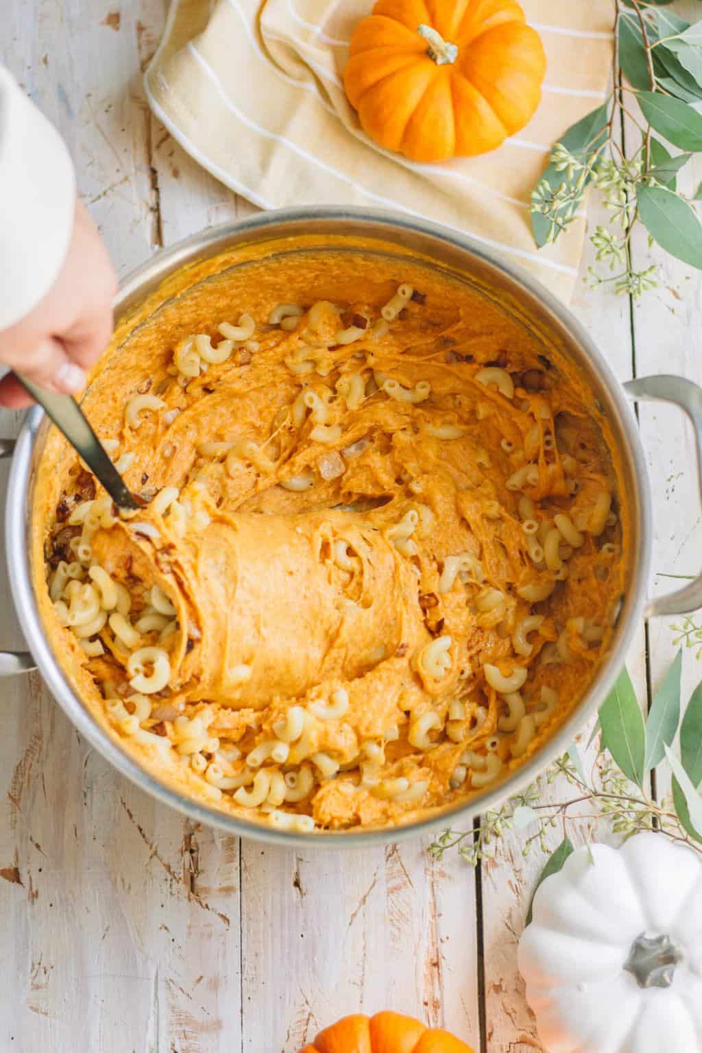 A pot of macaroni noodles being mixed with pumpkin cheese mixture.