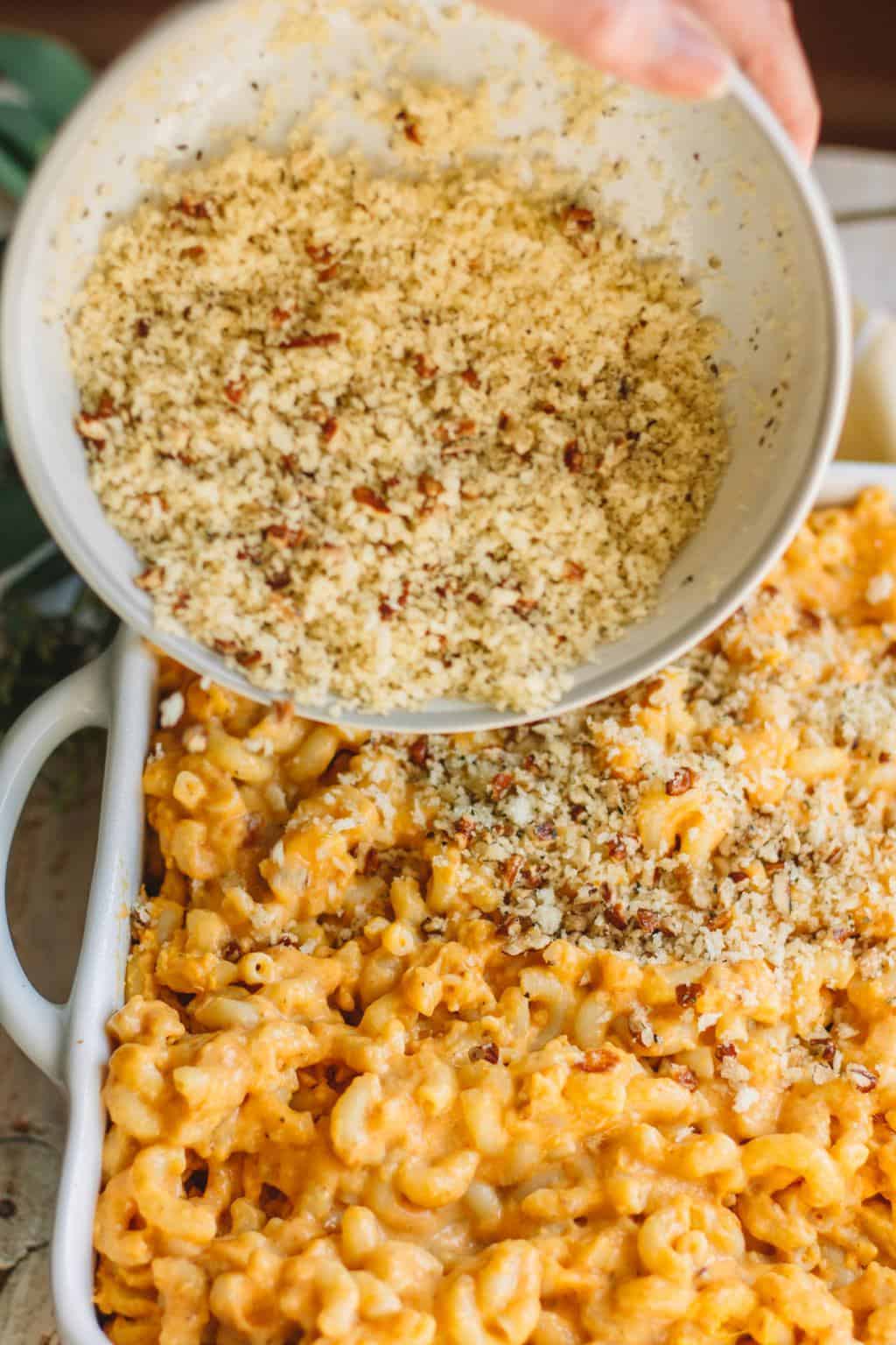 Pecan breadcrumb topping being poured on casserole dish of pumpkin mac and cheese.