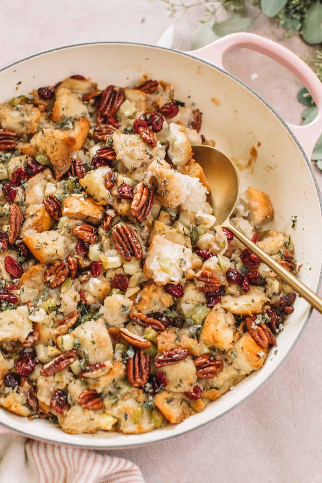 easy apple stuffing with pecans in pink casserole dish with gold serving spoon