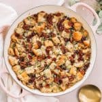 apple stuffing with pecans in pink casserole dish on kitchen towel with gold spoon