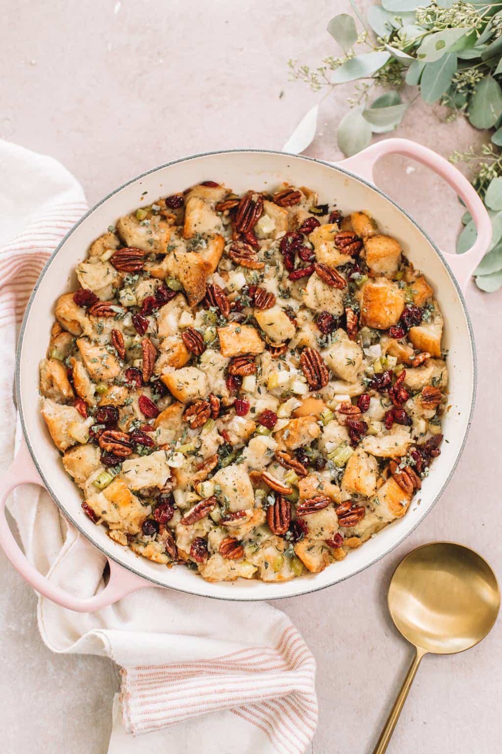 apple stuffing with pecans in pink casserole dish on kitchen towel with gold spoon