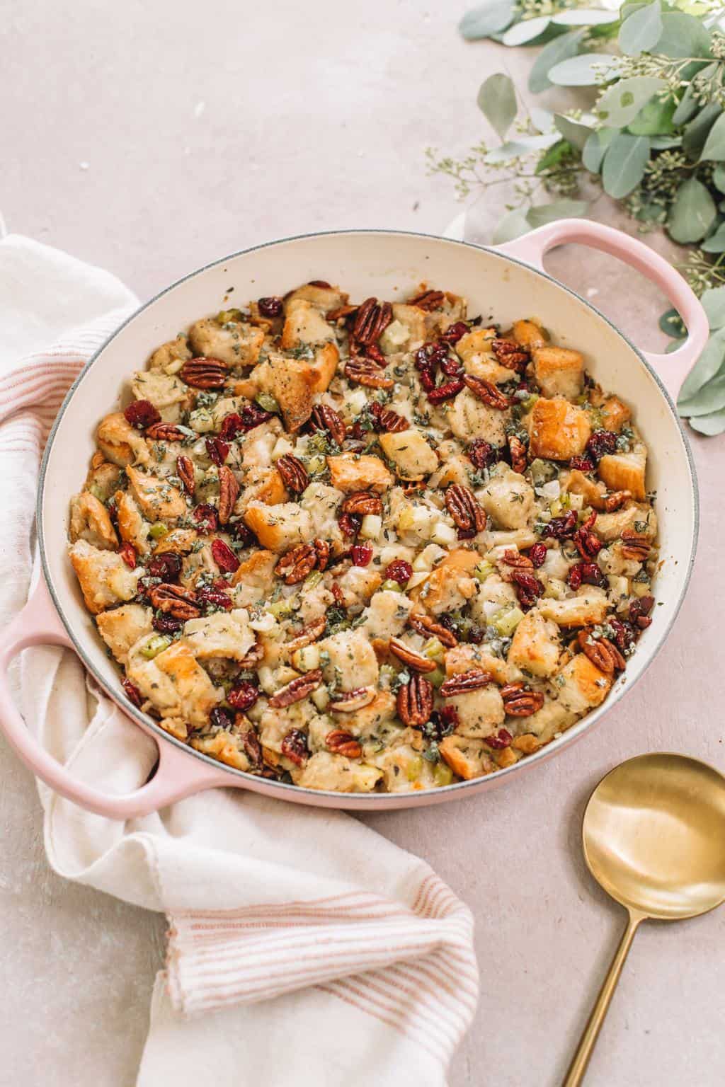 apple stuffing with pecans in pink casserole dish on kitchen towel with gold spoon