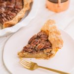 slice of pecan pie with homemade pie crust on white plate with gold fork