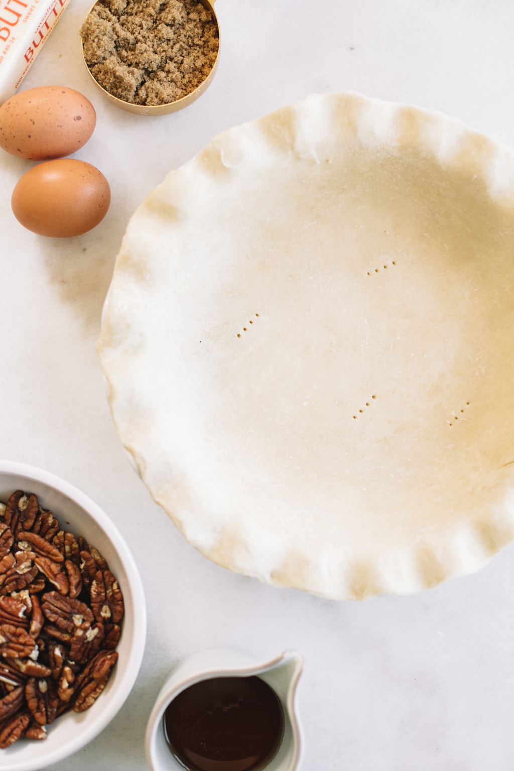 homemade pie crust in white pie dish with two eggs and pecans in white bowl