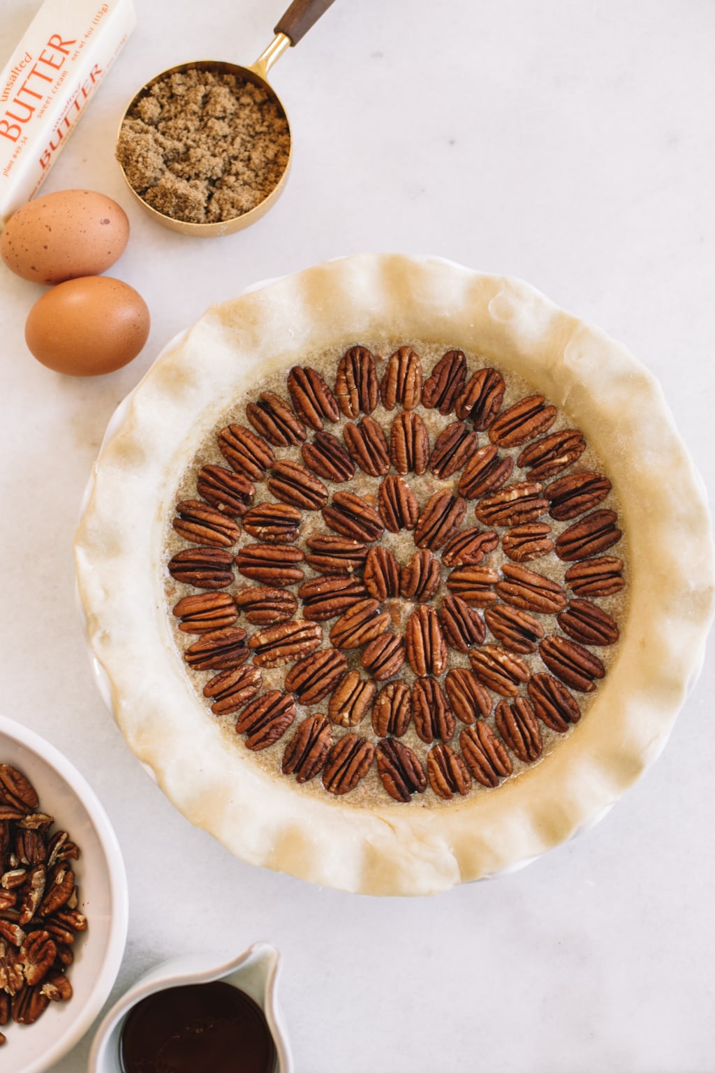 pecans placed in concentric circles in homemade pie crust in white pie dish with two eggs on the side