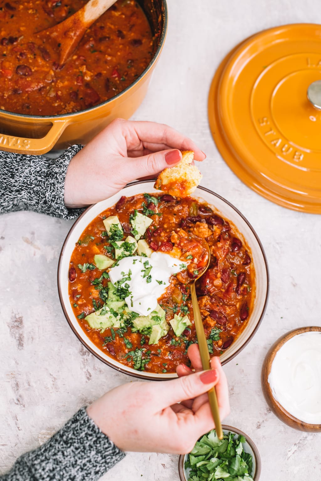 hand dipping cornbread in chipotle turkey chili in white bowl with gold spoon