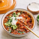 chipotle turkey chili in white bowl with gold spoon with yellow dutch oven lid