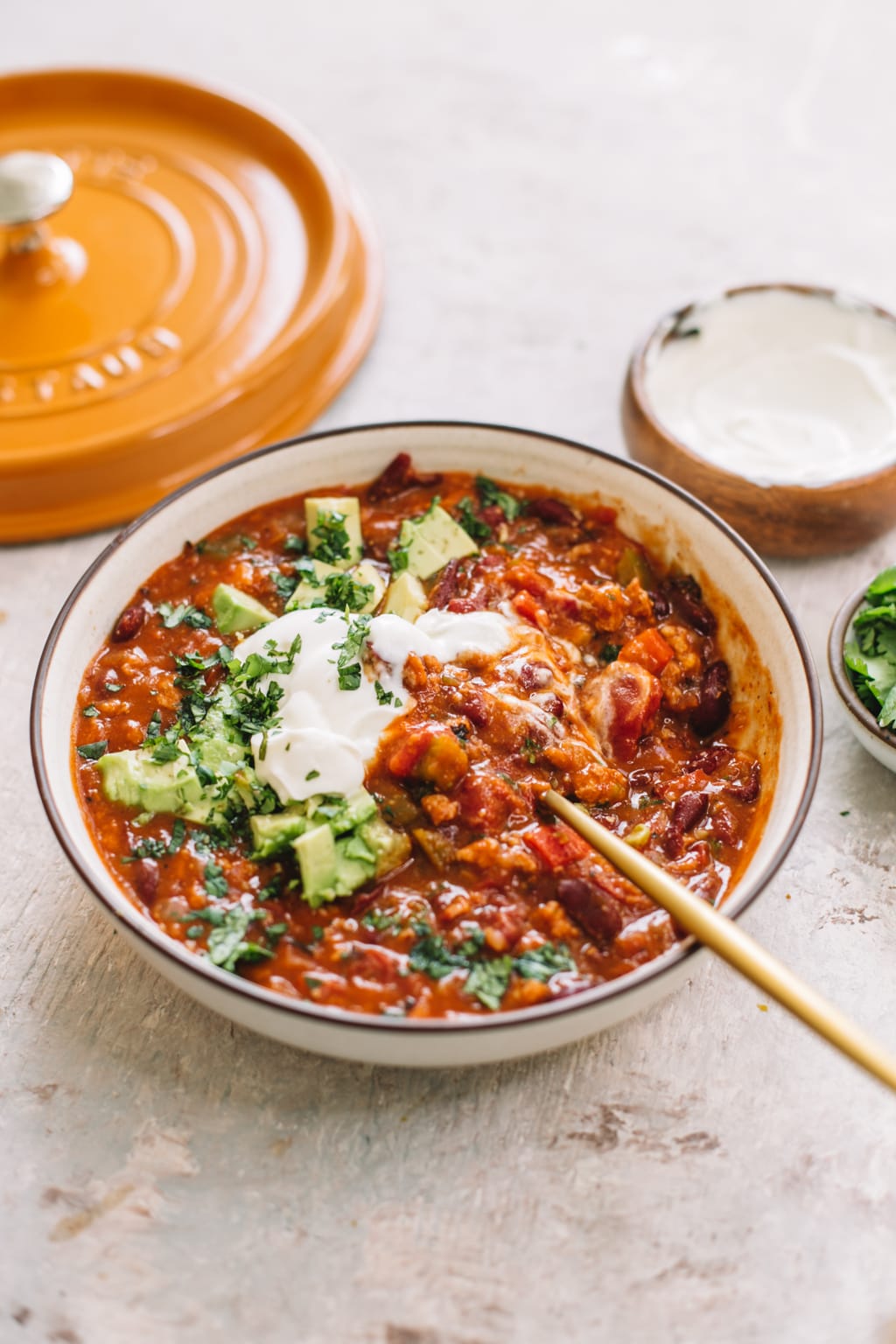 chipotle turkey chili in white bowl with gold spoon with yellow dutch oven lid