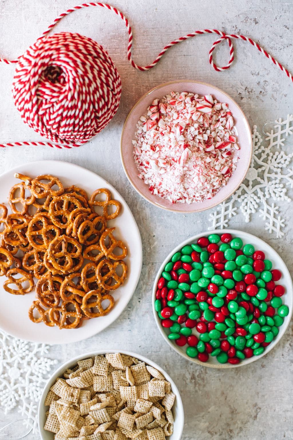 rice chex cereal, Christmas m&ms, mini salted pretzels, crushed peppermint candy in white bowl with ribbon